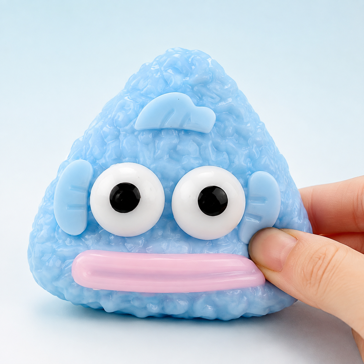 Hand pressing a blue funny-fish rice-ball sensory squeeze toy