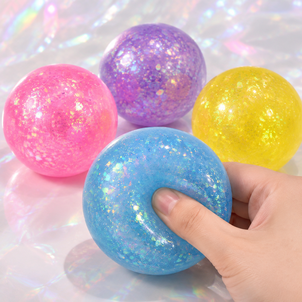 Four glitter ball colors with a hand pressing the blue ball