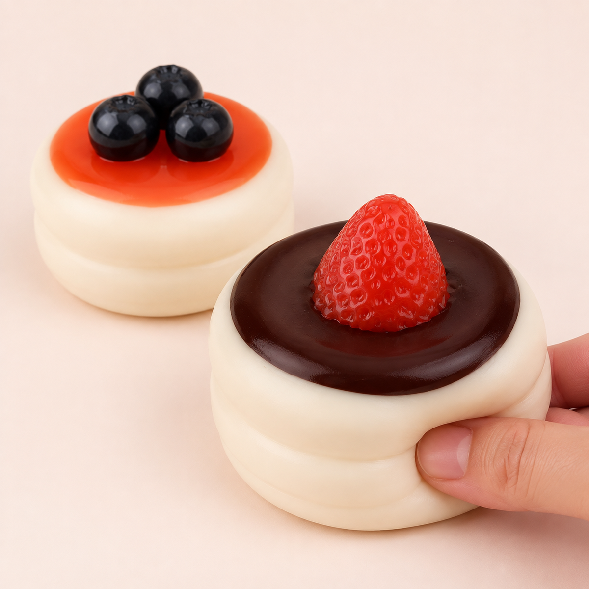 Hand pressing strawberry soufflé squeeze toy beside blueberry variant