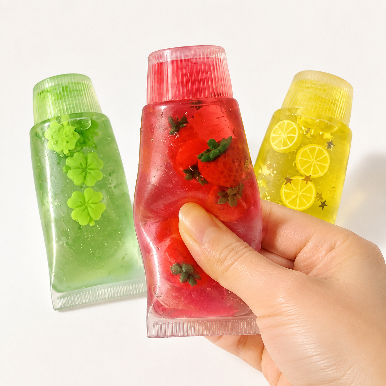 Hand pressing strawberry tube beside clover and lemon sensory toys