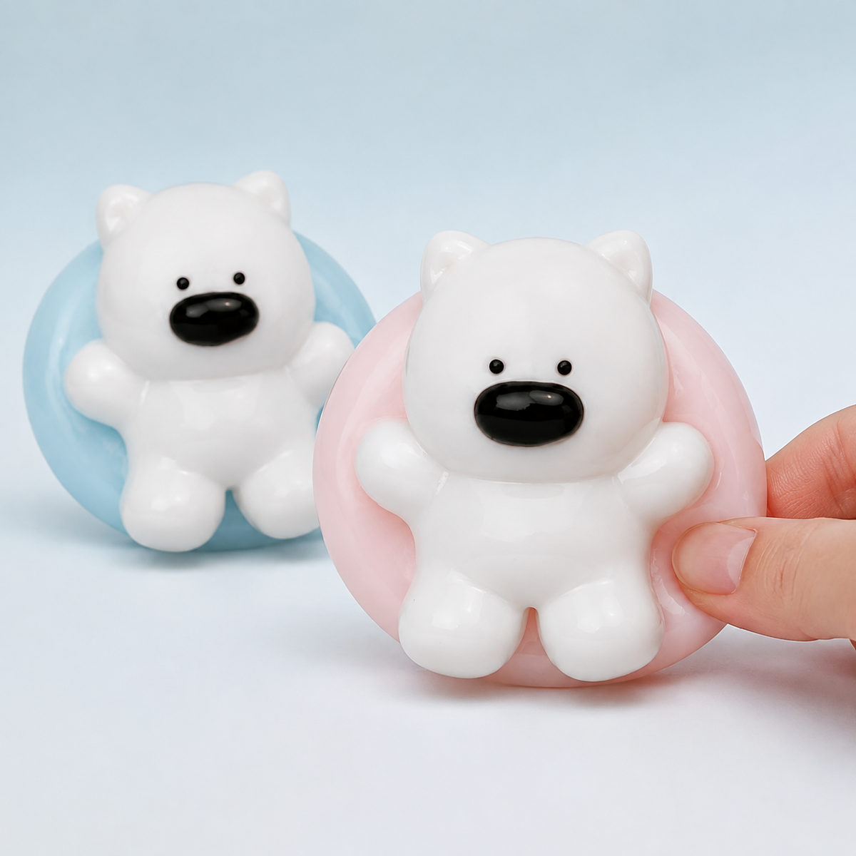 Hand pressing the pink Westie swim-ring squeeze toy beside blue variant
